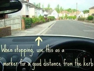 View from the driver's seat through the front windscreen, with an arrow marking the reference point at the base of the windscreen that lines up with the kerb. Text on the photo reads: When stopping, use this as a marker for a good distance from the kerb.